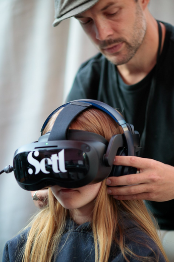 Child wearing Setl virtual reality headset, man standing behind her adjusting the headset